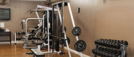 A gym with weightlifting equipment, a bench, and a rack of dumbbells.