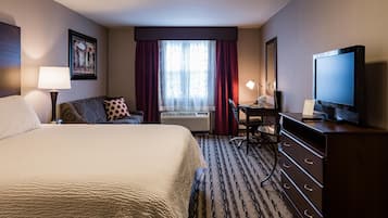A hotel room with a large bed, a desk, a television, and a window with curtains.