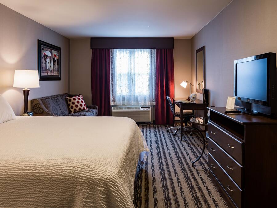 A hotel room with a large bed, a desk, a television, and a window with curtains.