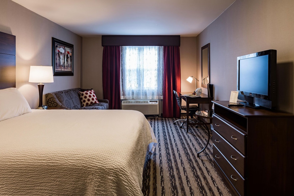 A hotel room with a bed, a desk, a television, and a dresser.