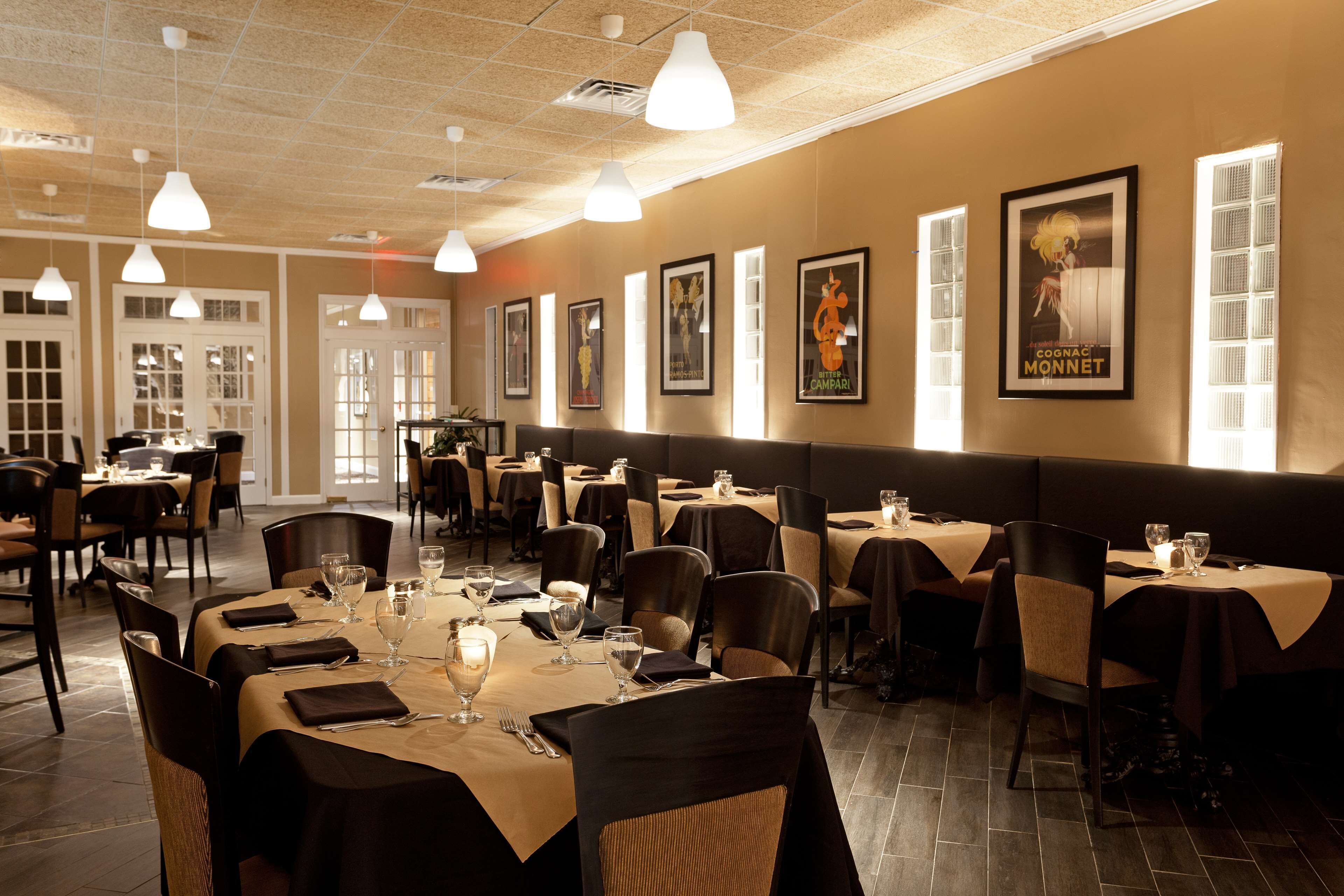 Um restaurante com mesas montadas para refeições, obras de arte emolduradas nas paredes e iluminação pendente.