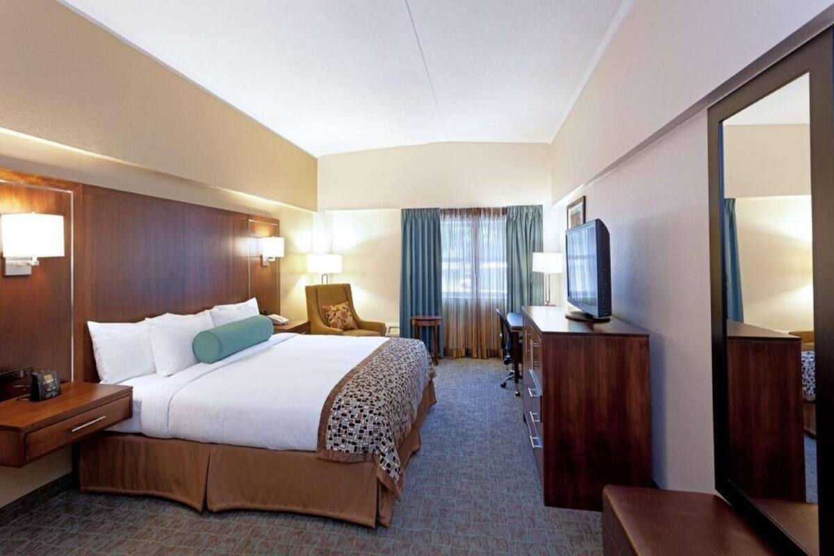 A hotel room with a large bed, bedside tables, a desk with a chair, a television, and a mirror.