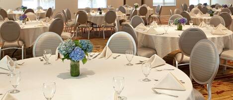 A banquet hall with round tables, chairs, and chandeliers.