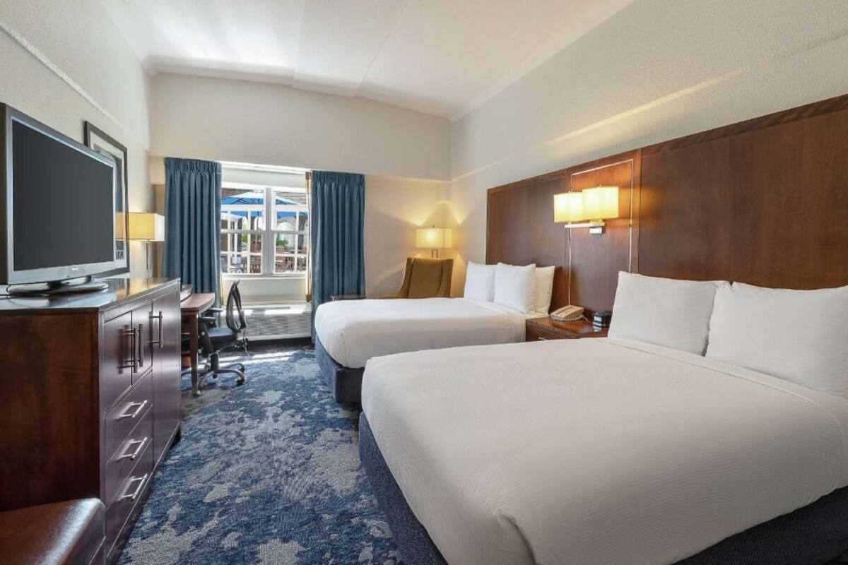 A hotel room with two beds, a TV, a desk, and a window with curtains.