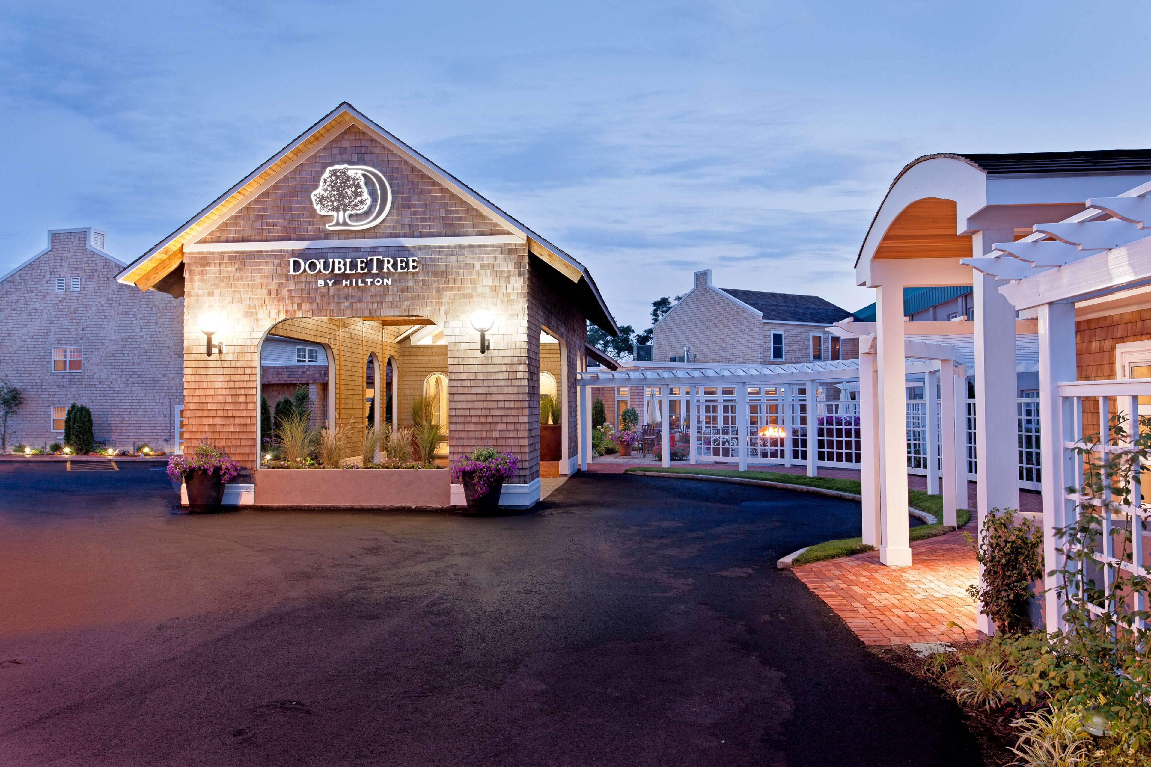 Entrada a un hotel DoubleTree by Hilton con fachada de ladrillo, señalización iluminada y un corredor cubierto.