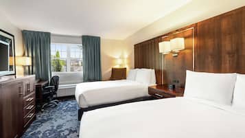 A hotel room with two beds, a desk, a chair, and a large window with curtains.