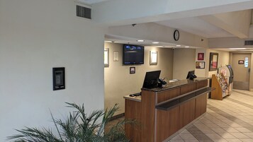 Zona de recepción de un hotel con mostrador de recepción, televisor de pantalla plana, reloj y letrero de Red Roof.