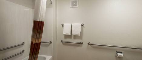 Un baño con bañera, cortina de ducha, toallero con dos toallas, baranda y dispensador de papel higiénico.