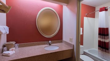 Une salle de bain avec un comptoir en granit, un miroir rond, un lavabo blanc, des toilettes et un rideau de douche.