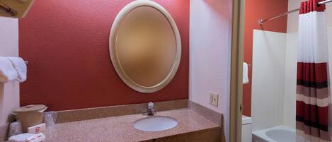 A bathroom with a granite countertop, a round mirror, a white sink, a toilet, and a shower curtain.