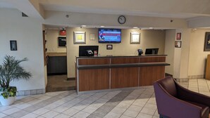 A reception area with a wooden counter, a digital screen, a clock, and a potted plant. - Red Roof Inn San Antonio - Airport (San Antonio)