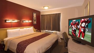 Hotellihuone, jossa on sänky, televisio, josta näkyy urheilulaji, työpöytä ja tuoli.