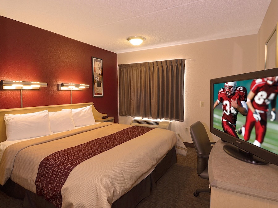Habitación de hotel con cama, televisor mostrando un partido deportivo, escritorio y una silla.