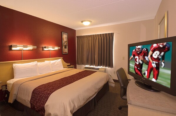 Habitación de hotel con cama, televisor mostrando un partido deportivo, escritorio y una silla.