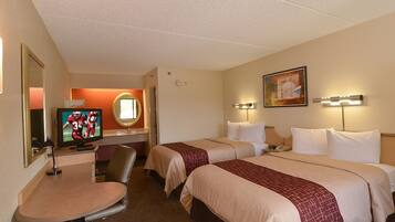 Ein Hotelzimmer mit zwei Betten, einem Schreibtisch mit Stuhl, einem Fernseher und einem Spiegel.
