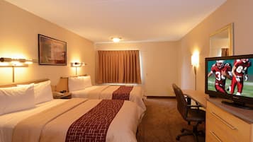 A hotel room with two beds, a desk, a television, and a window with curtains.