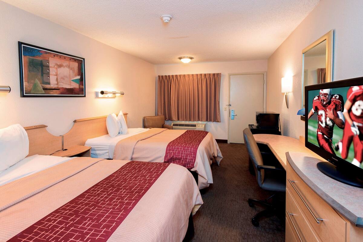 Quarto de hotel com duas camas, uma escrivaninha, televisão e um quadro na parede.