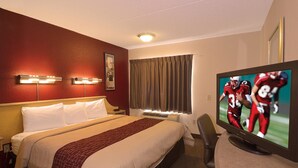 Quarto de hotel com cama, televisão, escrivaninha e janela com cortinas.