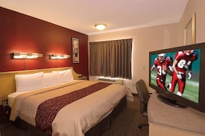 A hotel room with a bed, a TV, a desk, and a window with curtains.