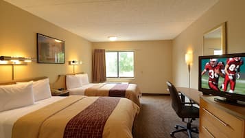 A hotel room with two beds, a desk, a television, and a window with curtains.