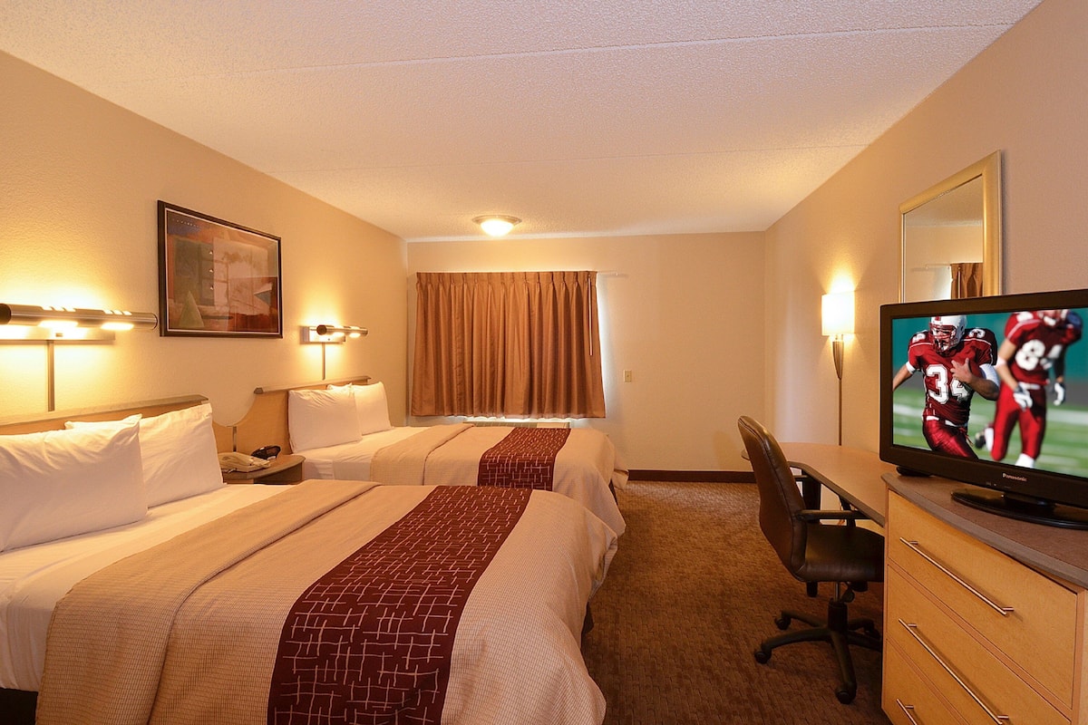 A hotel room with two beds, a desk, a television, and a mirror.
