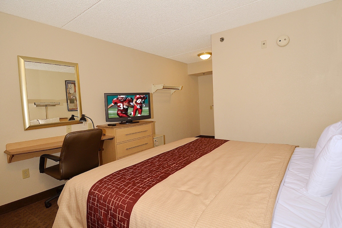 A hotel room with a bed, a desk with a chair, a television, and a mirror.