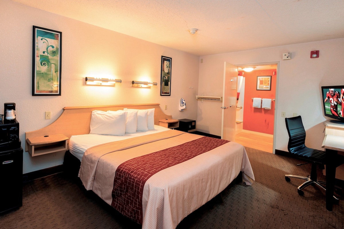 A hotel room with a large bed, bedside tables, a desk with a chair, and a television.
