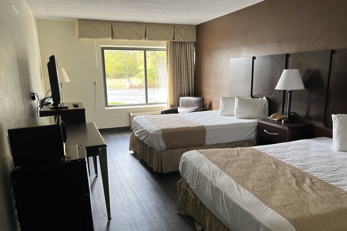 A hotel room with two beds, a desk, a chair, a TV, and a window with curtains.