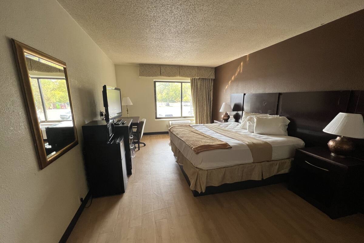 A hotel room with a bed, desk, chair, and a large window.