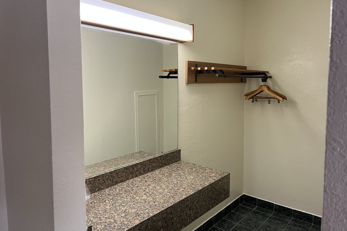A bathroom with a granite countertop, a mirror, a wooden towel rack, and a door.