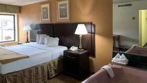 A hotel room with a large bed, two bedside lamps, a nightstand with a telephone, a mirror, and a bathroom with a sink and towel stack.