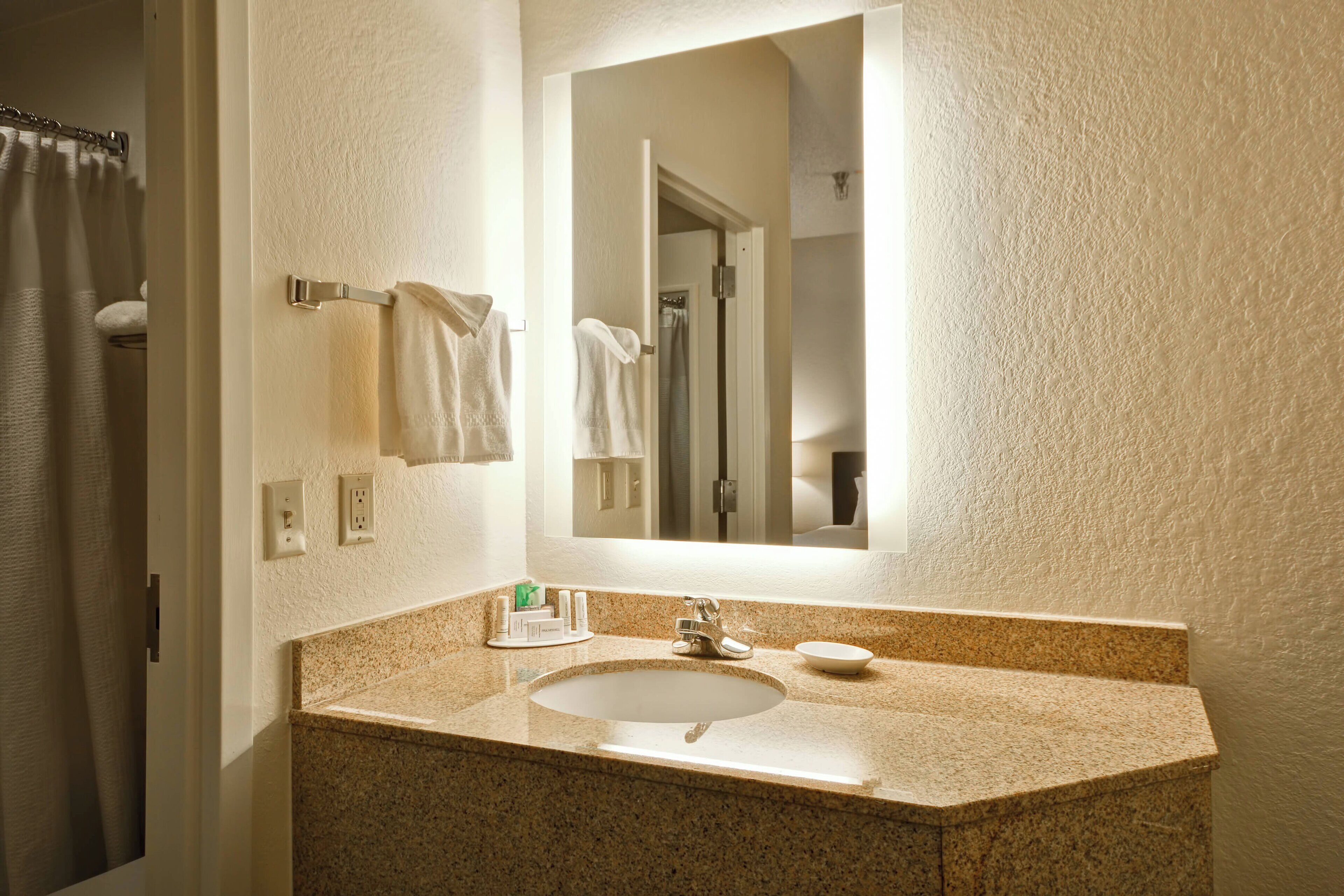 A bathroom with a granite countertop sink, a mirror, and a towel rack.