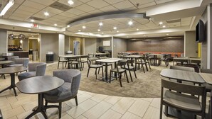 A spacious indoor dining area with multiple tables and chairs, a kitchen area in the background, and an exit sign on the ceiling.