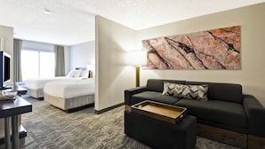A hotel room with a bed, a sofa, a desk, and a large abstract painting on the wall.