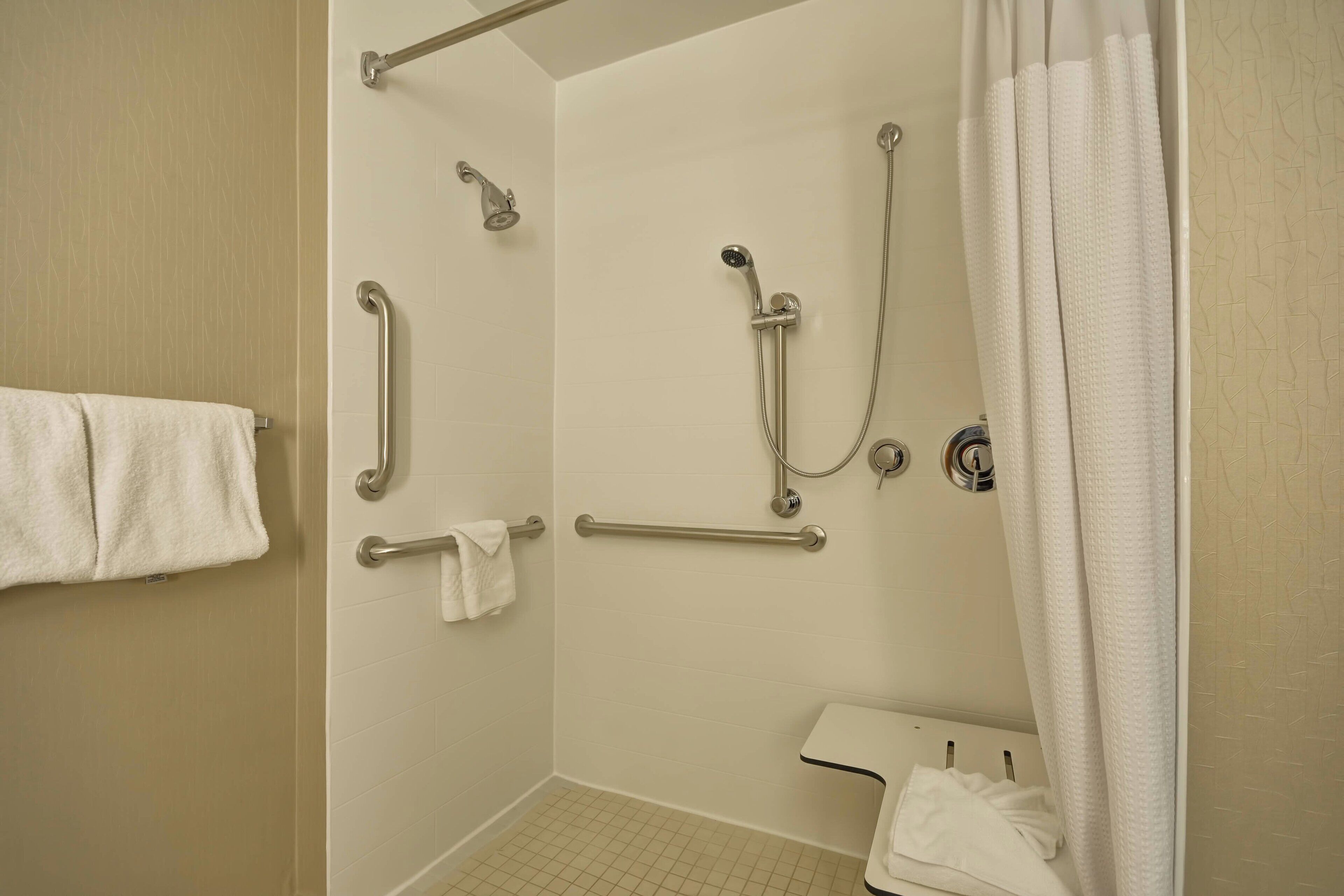 A shower area with grab bars, a handheld showerhead, and a white shower curtain.