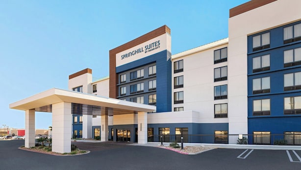 A modern hotel with a prominent signage for Springhill Suites by Marriott, featuring a multi-story structure with a flat roof and a covered entrance area.