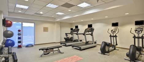 A gym with treadmills, elliptical machines, free weights, and exercise balls.