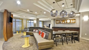 A modern hotel lobby with a curved sofa, dining area, and a TV mounted on a wooden panel.