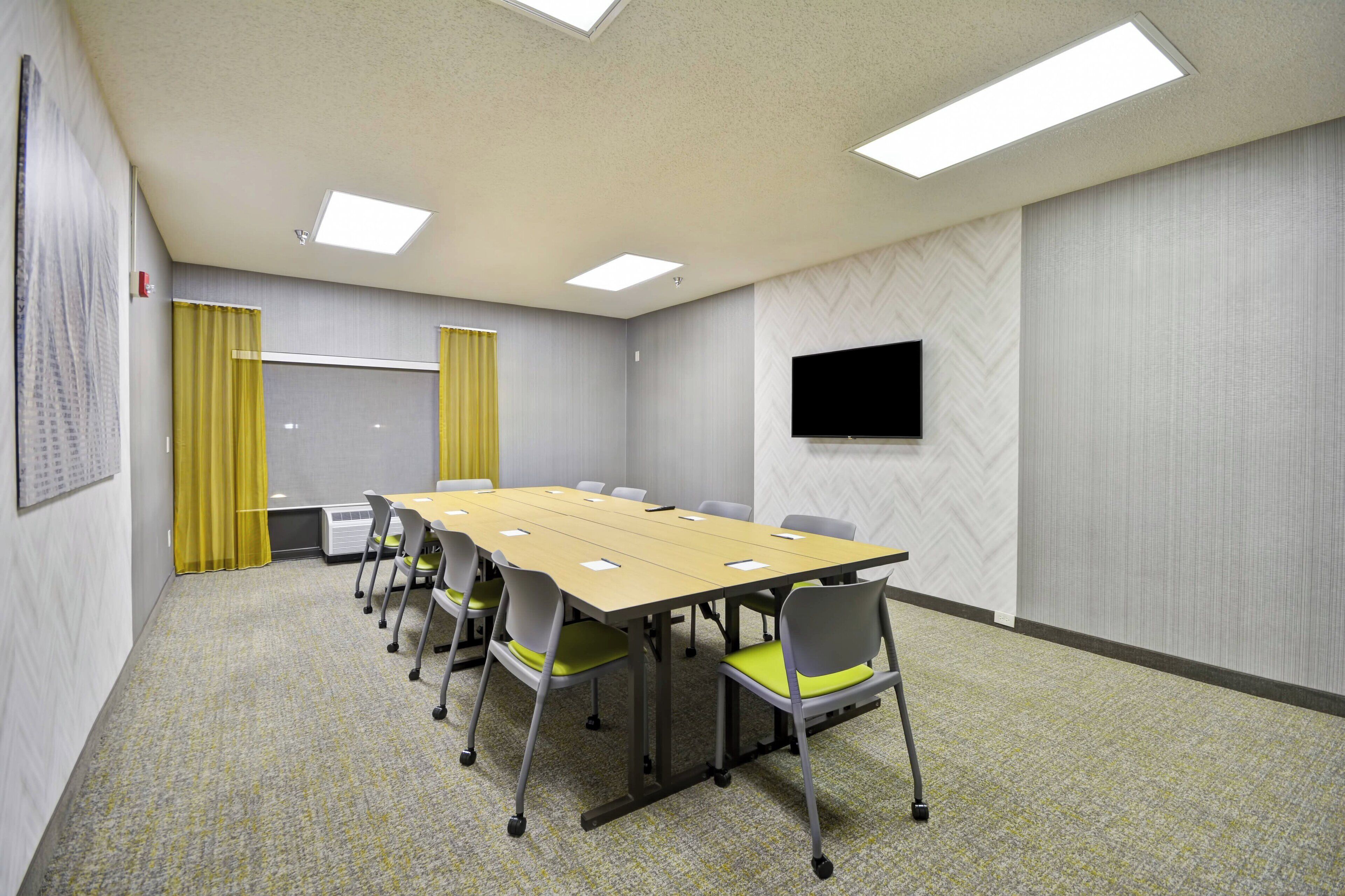A conference room with a long table, six chairs, and a flat-screen TV on the wall.