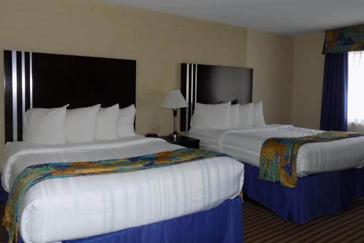 Habitación de hotel con dos camas, una mesita de noche, una lámpara y una ventana con cortinas.