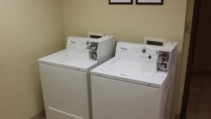 Two Whirlpool front-loading washers in a laundry room with beige walls and tiled flooring. - Rodeway Inn (Portage)