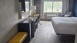 A hotel room with a bed, desk, chair, and a small bench. - Rodeway Inn (Portage)