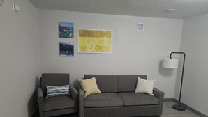 A room with two grey sofas, a floor lamp, and two wall-mounted paintings. - Rodeway Inn (Portage)