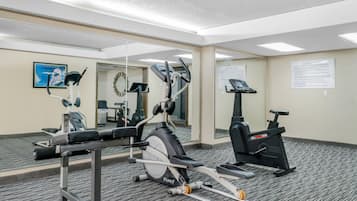 Un gimnasio con máquinas de cardio, espejos y carteles de ejercicios.