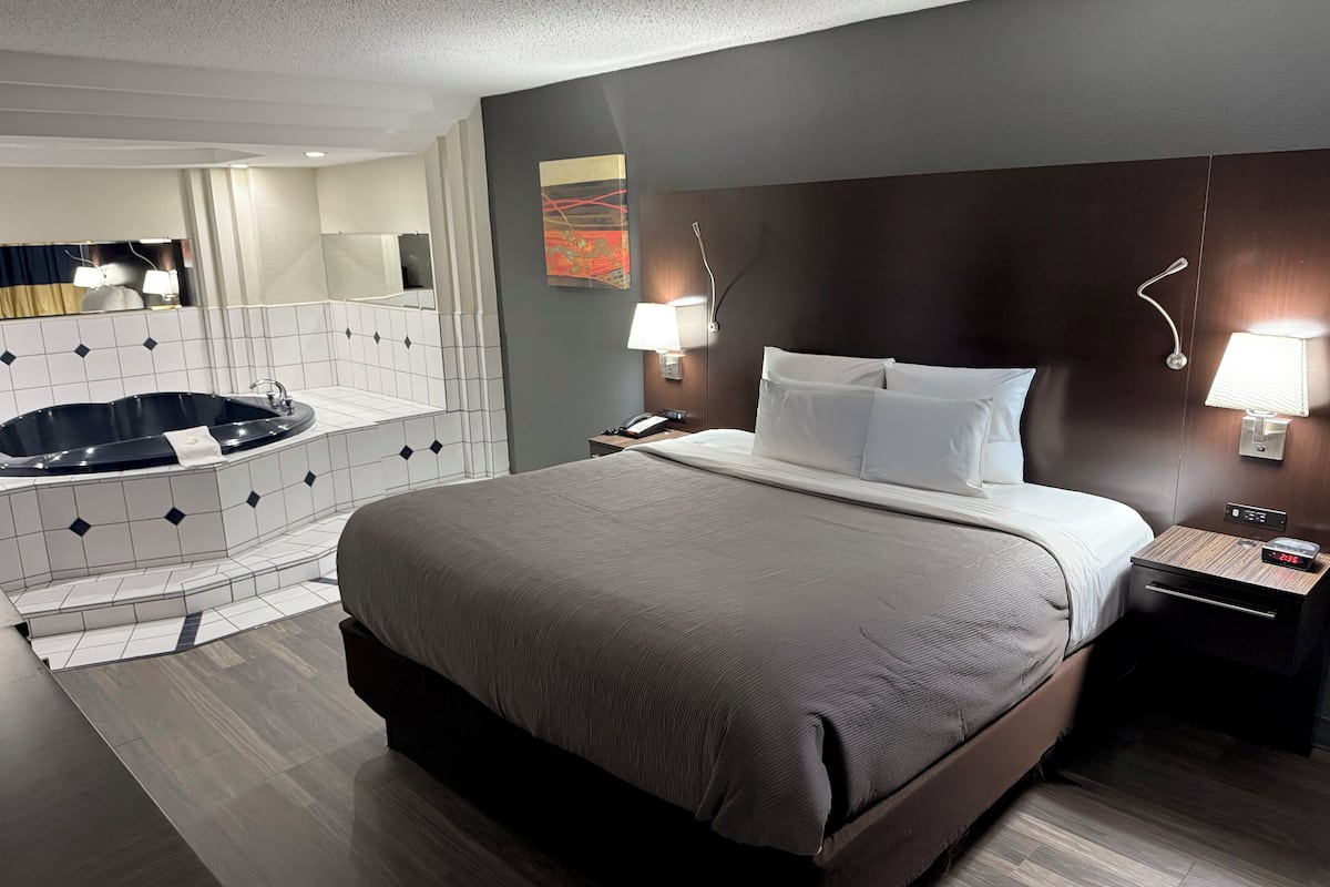 Une chambre d’hôtel avec un grand lit, une salle de bain séparée avec une baignoire, une table de chevet avec une lampe et une horloge fixée au mur.
