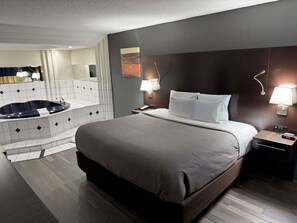 A hotel room with a large bed, a separate bathroom with a bathtub, a nightstand with a lamp, and a wall-mounted clock. - Quality Inn and Suites Livonia (Livonia)