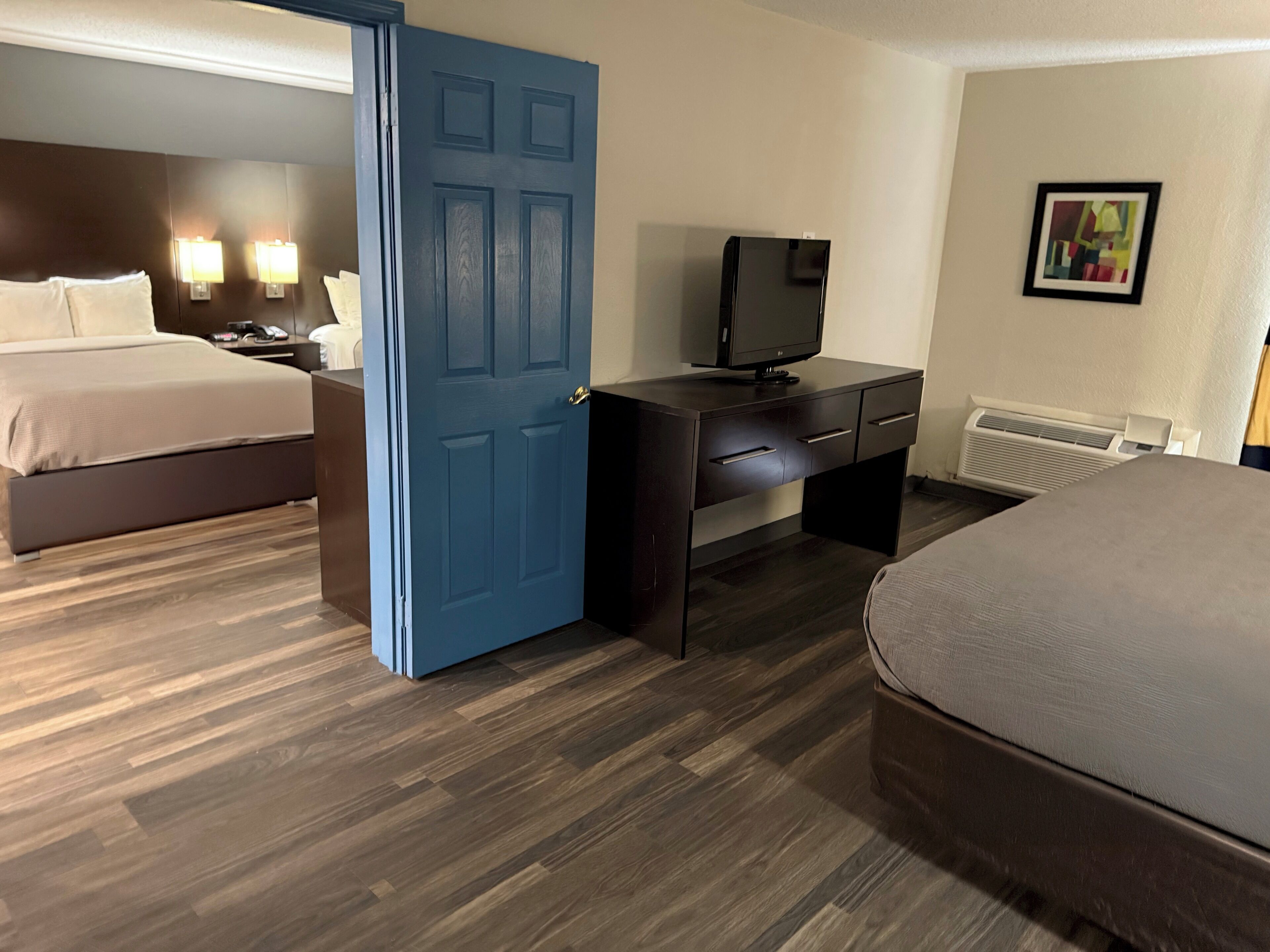 A hotel room with a bed, a desk with a television, and a wall-mounted heater.