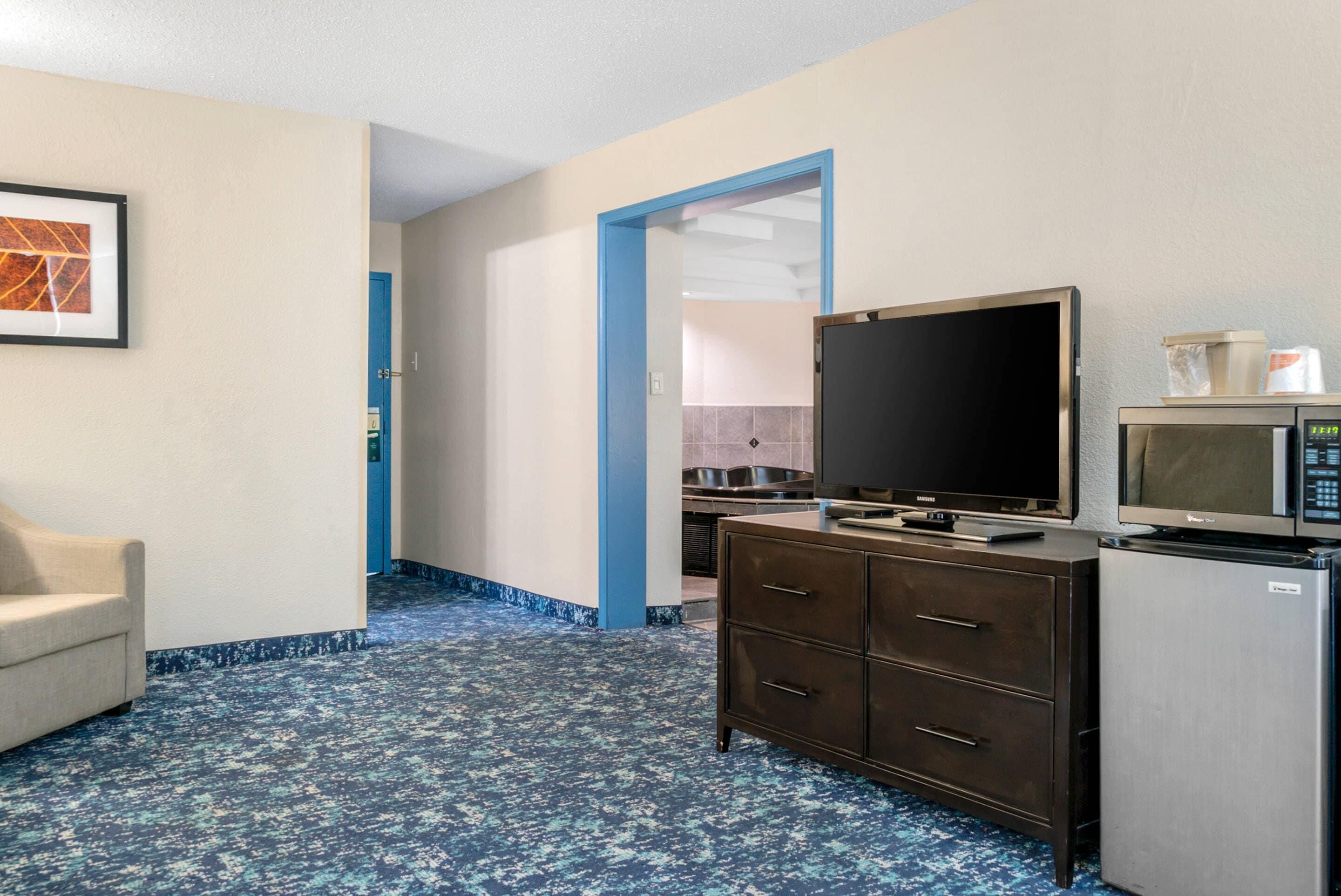 A hotel room with a flat-screen TV, a microwave, a refrigerator, a dresser, and a framed picture on the wall.