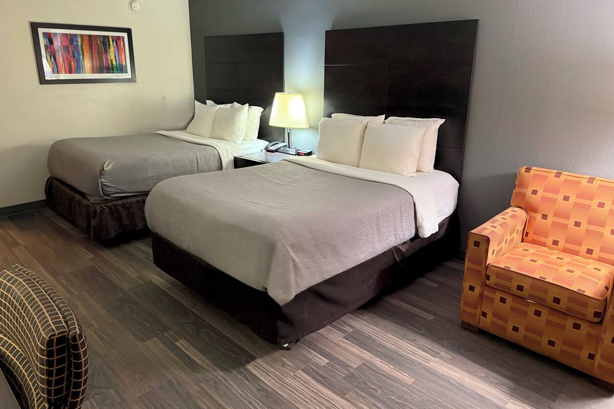 Une chambre d’hôtel avec deux lits, une chaise, une lampe et un tableau au mur.