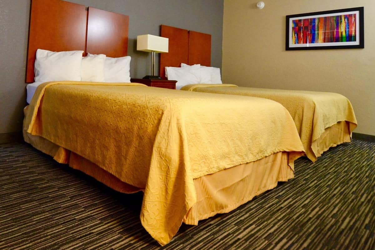 Une chambre d’hôtel avec deux lits, une table de chevet, une lampe et une peinture abstraite aux couleurs vives accrochée au mur.